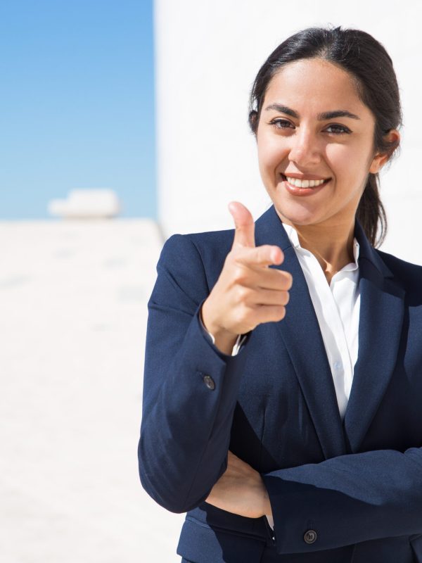 Happy ambitious HR manager choosing you. Confident young business woman in formal suit standing outside with arms folded and pointing finger at camera. Human resource or career concept